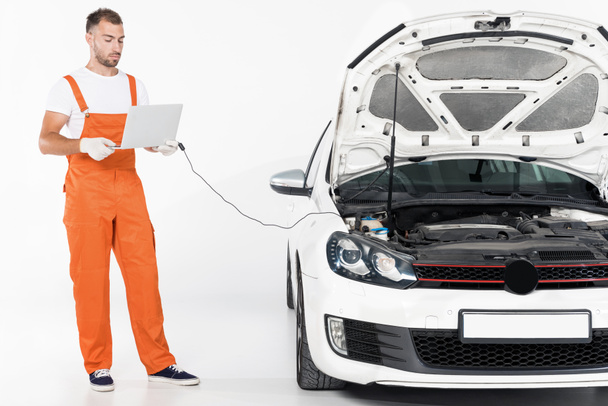 handsome auto mechanic checking broken car with laptop on white - Foto, Imagem