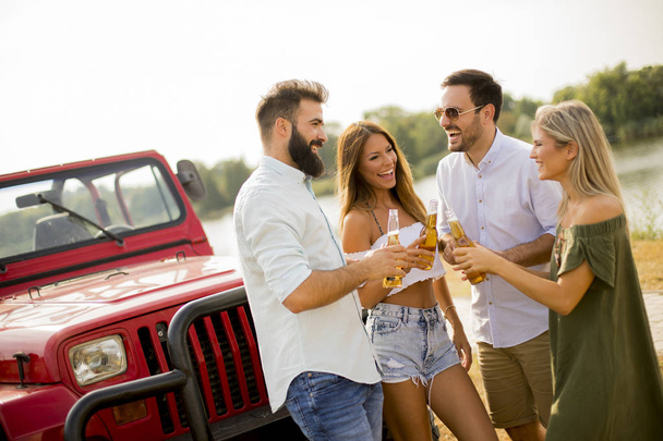 Jugendliche trinken und amüsieren sich an heißen Sommertagen im Freien mit dem Auto - Foto, Bild