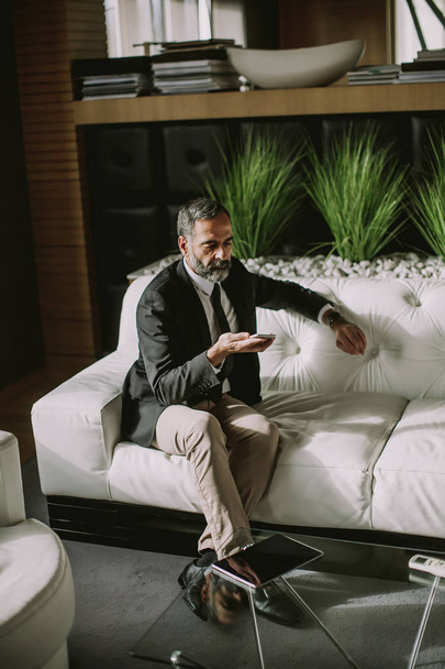 schöner Geschäftsmann mittleren Alters mit Handy im modernen Büro auf dem Sofa - Foto, Bild