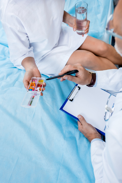 image recadrée du médecin d'âge moyen avec stéthoscope au-dessus du cou pointant vers les pilules pour patiente dans la chambre d'hôpital
  - Photo, image