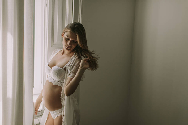Pretty young pregnant woman standing by the window - Фото, изображение