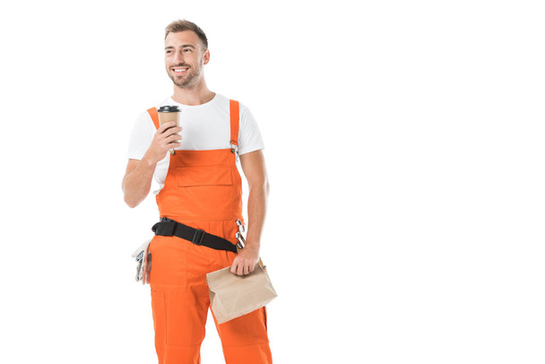 handsome auto mechanic holding coffee to go and paper bag with lunch isolated on white - Φωτογραφία, εικόνα