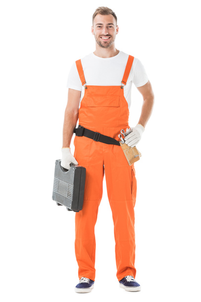smiling handsome auto mechanic in orange uniform holding toolbox isolated on white - 写真・画像