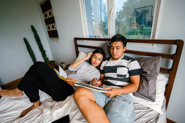 Portrait of a young and attractive Malay Asian couple sitting around lazily in bed on the weekend.  - Foto, Imagen