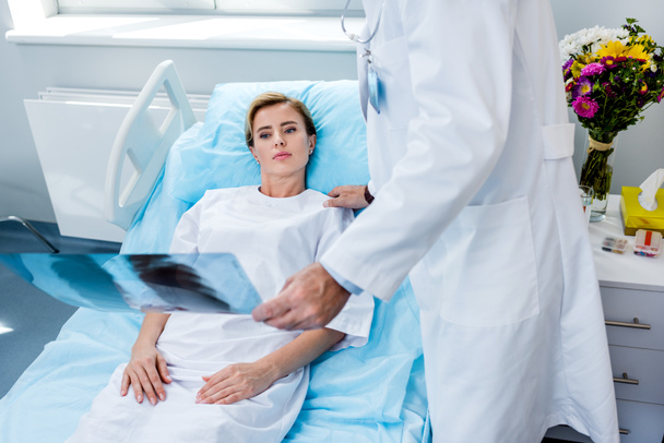 bijgesneden afbeelding van mannelijke arts holding x-ray foto en gejuich van vrouwelijke patiënt in ziekenhuis kamer - Foto, afbeelding