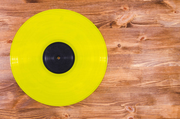 Disque vinyle de couleur jaune avec étiquette noire sur fond brun en bois
 - Photo, image