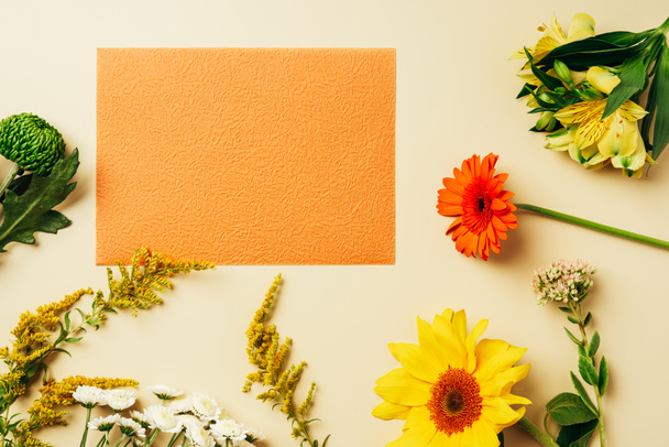 flat lay with various wildflowers around blank orange card on beige background - Foto, Bild