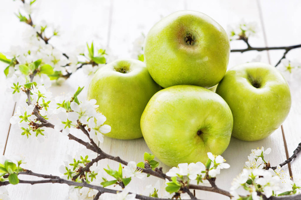 Manzanas verdes maduras con flores de primavera sobre un fondo de madera blanca. Fondo de alimentos ligeros, fruta fresca, manzanas
 - Foto, Imagen