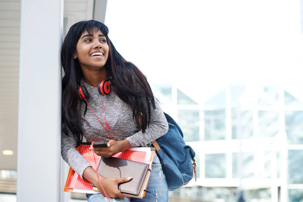 Портрет улыбающейся студентки с мобильным телефоном, книгами и сумкой
 - Фото, изображение