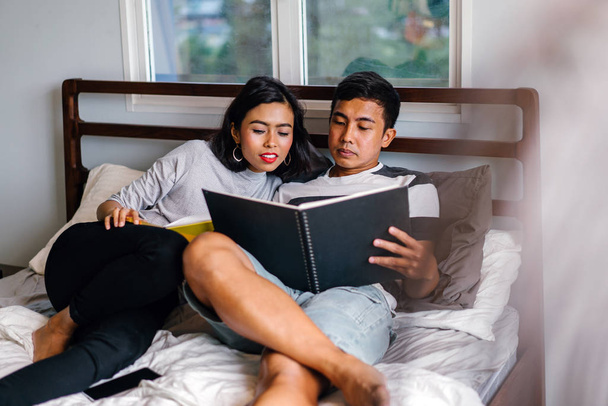 Portrait of a young and attractive Malay Asian couple sitting around lazily in bed on the weekend.  - Foto, afbeelding