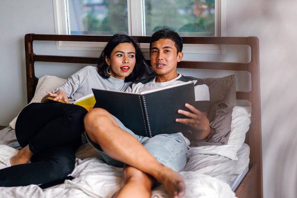 Portret van een jonge en aantrekkelijke Maleis Aziatische paar rondhangen lui op bed in het weekend.  - Foto, afbeelding