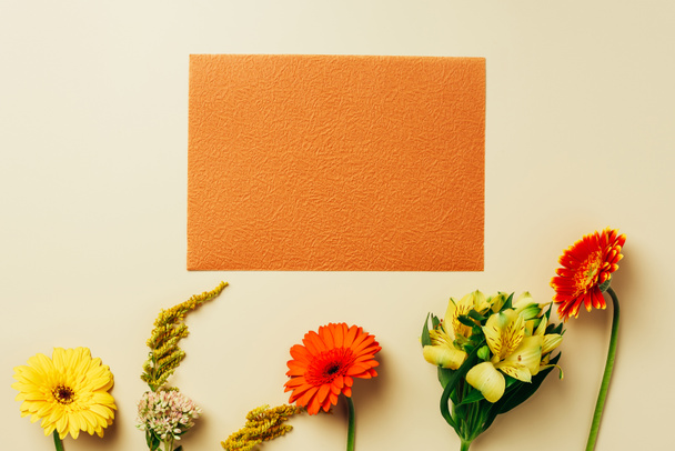 flat lay with beautiful flowers and empty orange card arrangement on beige backdrop - Photo, Image