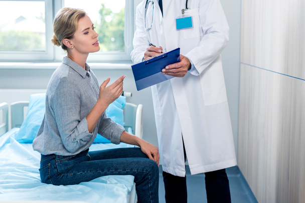 περικομμένη εικόνα του αρσενικό ο γιατρός δείχνει Πρόχειρο σε γυναίκα ασθενή στο δωμάτιο του νοσοκομείου - Φωτογραφία, εικόνα