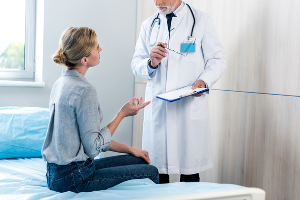 vrouwelijke patiënt gebaren met de hand en praten met mannelijke arts met Klembord in ziekenhuis kamer - Foto, afbeelding
