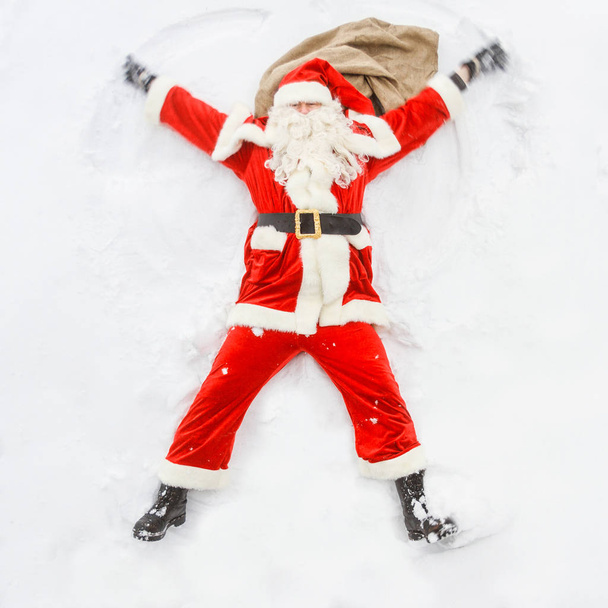Happy Santa Claus makes a snow angel in the snowfall. - Foto, afbeelding