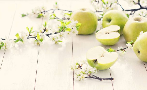 Ripe green apples with spring flowers on a white wooden background. Light food background, fresh fruit, apples - Photo, Image