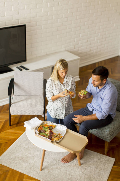 家庭でリラックスしておいしいピザを食べるカップルを愛する - 写真・画像