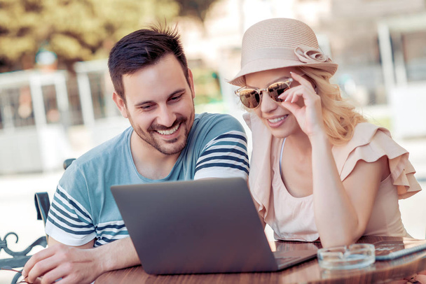 улыбающаяся молодая пара, сидящая за столом в кафе, глядя на ноутбук
 - Фото, изображение