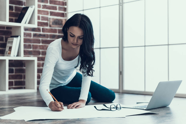 Young Woman Architect Drawing Blueprint at Home. Beautiful Female Architect Sitting on Floor next to Laptop and Drawing Blueprint of new Project. Woman Working Remotely in Home Office - Foto, Imagen