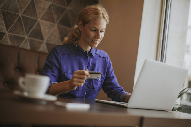 Blick auf junge Frau, die im Café sitzt, Kaffee trinkt und im Internet einkauft - Foto, Bild
