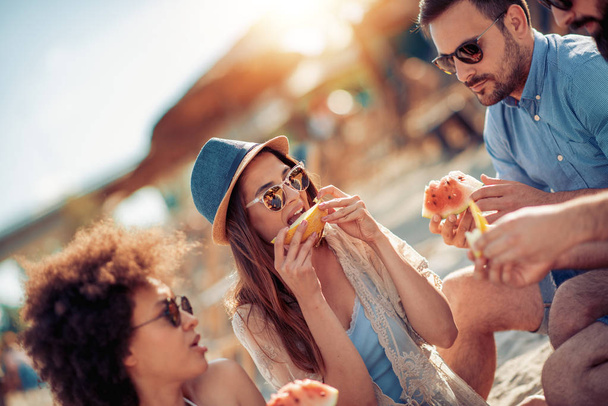 Щасливі молоді друзі розважаються на пляжі і їдять кавун
. - Фото, зображення