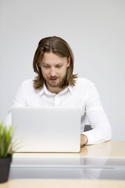 Όμορφος νεαρός άνδρας, που εργάζεται σε φορητό υπολογιστή στο γραφείο - Φωτογραφία, εικόνα