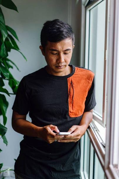 Portrait of a Malay Asian man standing near window and holding smartphone  - Foto, imagen