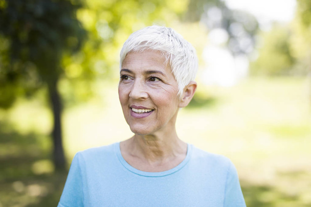Portréja egy mosolygó sportos idősebb nő, egy parkban, a nyári nap - Fotó, kép