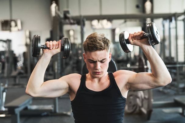 Young fit man in gym exercising with dumbbells. - Foto, afbeelding