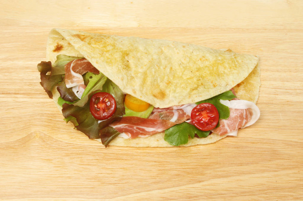 Piada flatbread filled with salad and parma ham on a wooden chopping board - Zdjęcie, obraz