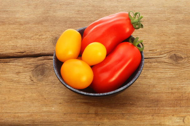 Homegrown red and yellow tomatoes in a bowl on rustic wood - Foto, afbeelding