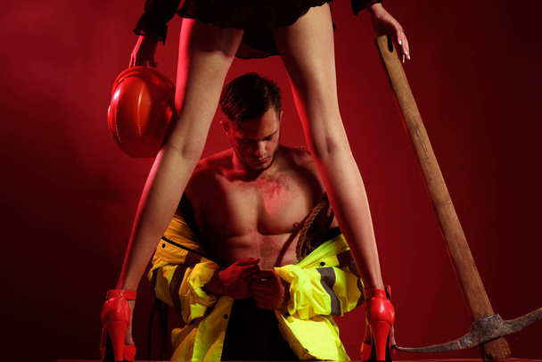 Brave Firefighter. Firefighter sexy body muscle man holding saved sexy woman. Rescuer firefighter or miners - risky occupations concept. Working profession, special clothes, overalls. Hot and sexy. - Zdjęcie, obraz