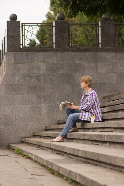 positive Frau sitzt und liest ein Buch auf den Stufen - Foto, Bild