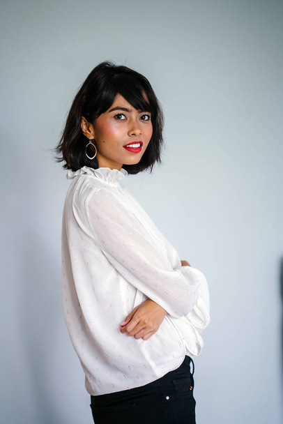 Portrait of a young, tall and slim Malay woman in a white shirt and black pants against a white background - Фото, изображение