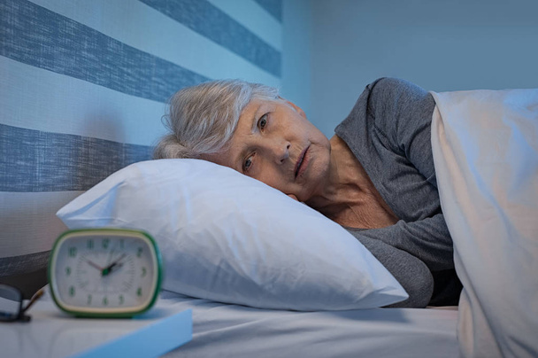 Worried senior woman in bed at night suffering from insomnia. Old woman lying in bed with open eyes. Mature woman unable to sleep at home. - Φωτογραφία, εικόνα