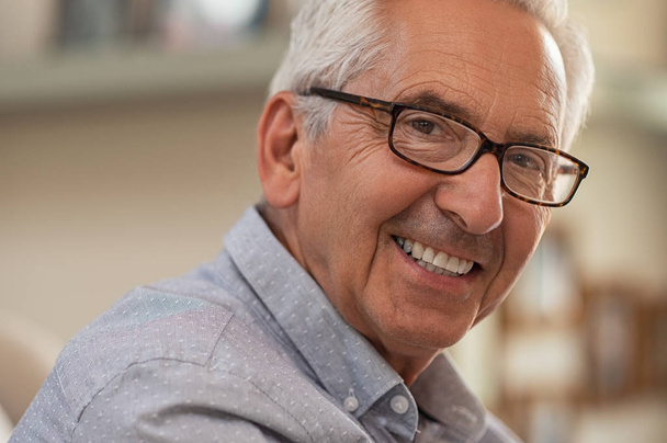 Portrait of smiling senior man with eyeglasses looking at camera. Successful mature man wearing spectacles at home. Closeup face of handsome elder with glasses and toothy smile. - 写真・画像
