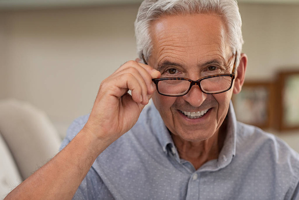 Portrait of happy mature man wearing spectacles and looking at camera. Old man smiling with glasses at home. Closeup face of elder trying new eyeglasses. - Fotó, kép