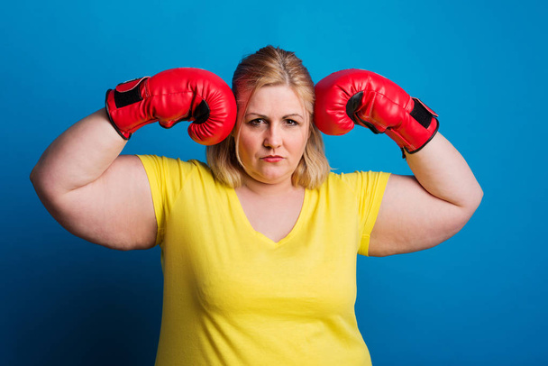 Portrait of an overweight woman with red boxing gloves in studio. - Foto, Bild