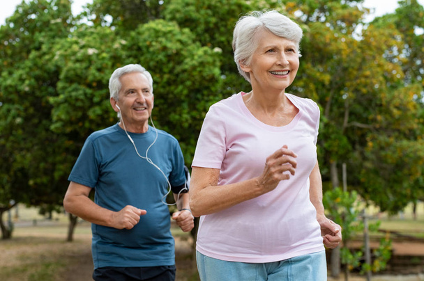 Senior couple running outside at park. Elderly man and old woman jogging together. Retired man and active woman exercising outdoor. - Foto, imagen