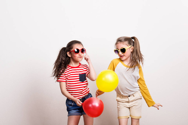 Small girls with sunglasses and balloons standing in a studio. - 写真・画像