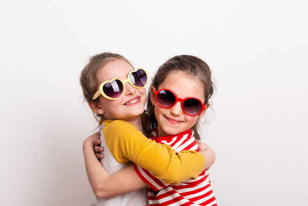 Small girls with sunglasses standing in a studio, hugging. - Zdjęcie, obraz