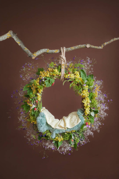 Ring with wildflowers hanging on a branch, pattern for photo shoots of newborns, brown background - Foto, afbeelding