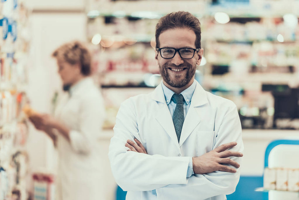 Portrait Smiling Pharmacist Working in Drugstore. Male Pharmacist wearing White Coat and Glasses Standing with hands crosed in Pharmacy. Professional Pharmacists at Work in Drugstore - Foto, Imagem