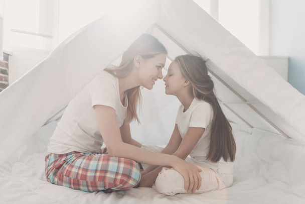 Young Happy Mother and Little Doughter Together. Beautiful Smiling Woman spending time with Cute Adorable Daughter. Mom and Child under tent in Bedroom. Family and Motherhood Concept - Фото, изображение