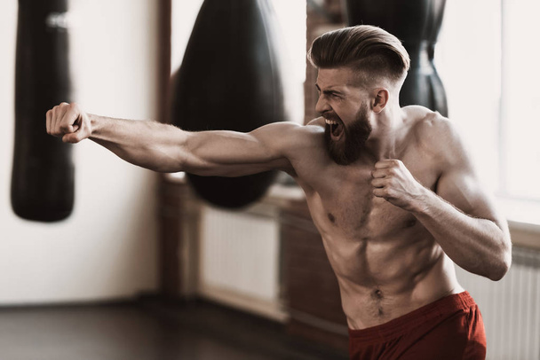 Athletic Male Boxer Training at Boxing studio. Portrait of Muscular Bearded Man during Exercise. Sporty Man during Boxing Exercise making direct Hit. Strength and Motivation Concept - Foto, afbeelding