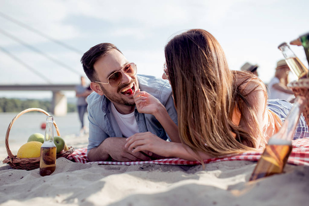 Portrait of happy couple on the beach,having fun.The girl feeds guy with cherries. - Photo, Image