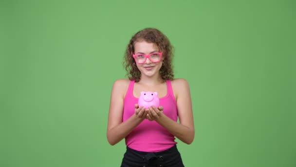 Young happy beautiful nerd woman giving piggy bank - Materiał filmowy, wideo