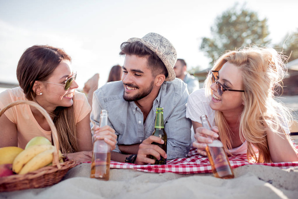 Léto, prázdniny, cestovní ruch, nápoje a lidé koncept skupina s úsměvem přátelé cinkání lahví piva na pláži. - Fotografie, Obrázek
