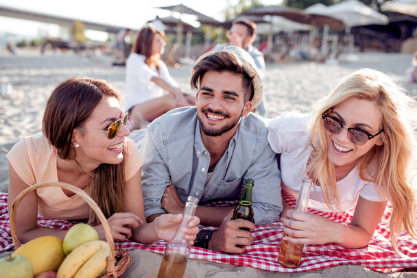 Verano, vacaciones, turismo, concepción de la gente- grupo de amigos sonrientes tintineando botellas de cerveza en la playa
. - Foto, imagen
