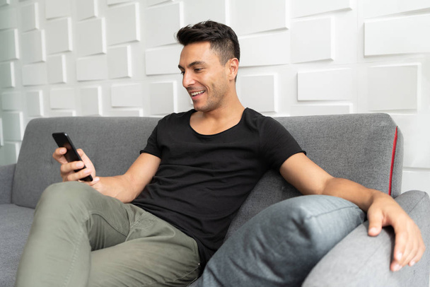 Portrait of Handsome man in casual is using smartphone and sitting on sofa. Happy young male relaxing. - Foto, Bild